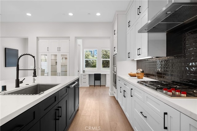 kitchen with wall chimney range hood, a sink, light countertops, stainless steel appliances, and white cabinetry