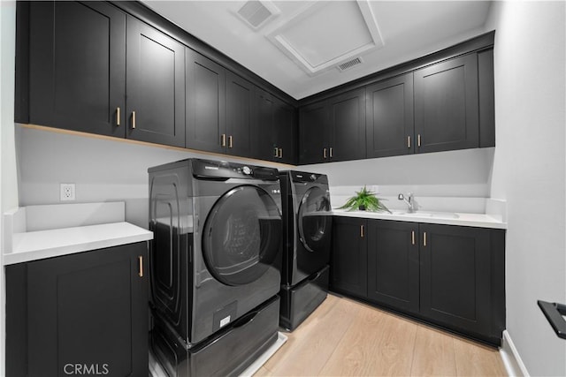 clothes washing area with cabinet space, washing machine and clothes dryer, a sink, light wood finished floors, and visible vents