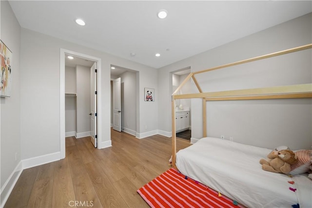 bedroom with baseboards, recessed lighting, wood finished floors, and a walk in closet