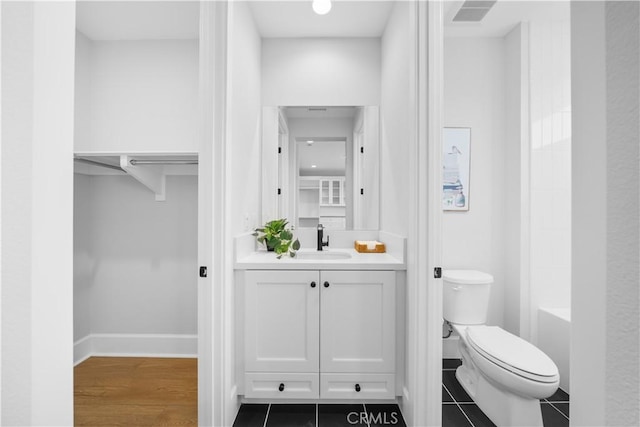bathroom with vanity, toilet, a tub, baseboards, and visible vents