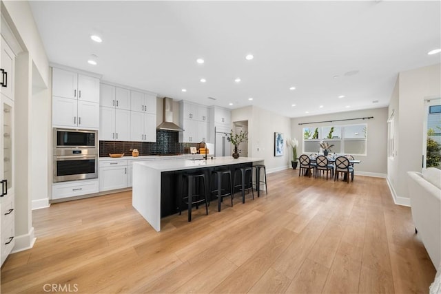 kitchen with wall chimney range hood, a kitchen bar, a center island with sink, a sink, and stainless steel oven