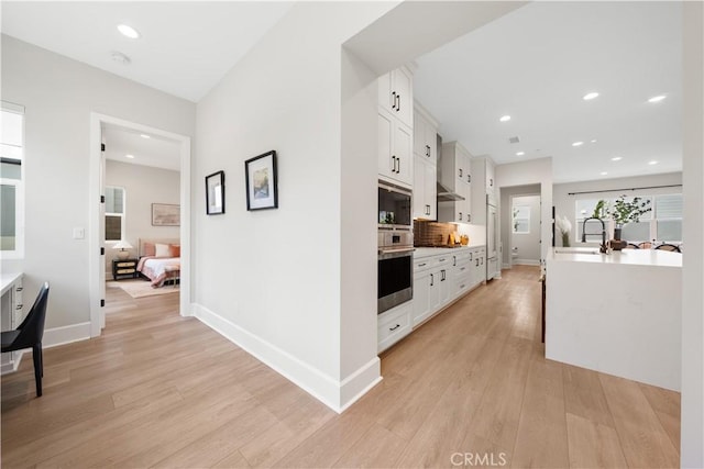 kitchen with a sink, built in appliances, white cabinets, and light wood finished floors