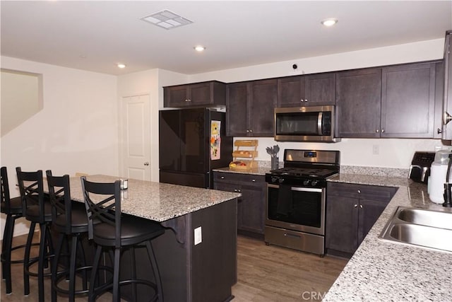 1322 Division Ct, Hemet, CA 92543 - kitchen with stainless steel appliances, wood finished floors, dark brown cabinets, a breakfast bar area, and light stone countertops