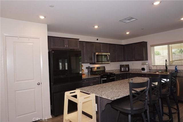 1322 Division Ct, Hemet, CA 92543 - kitchen with appliances with stainless steel finishes, a kitchen island, light stone counters, a kitchen bar, and dark brown cabinetry