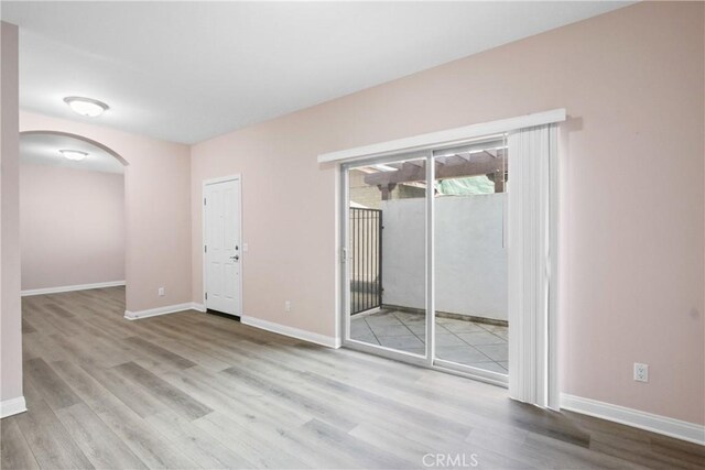 empty room featuring arched walkways, baseboards, and wood finished floors