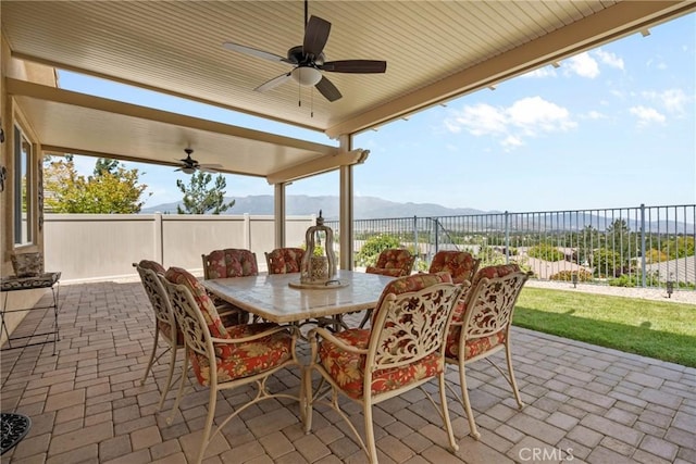 view of patio featuring outdoor dining area, fence, a ceiling fan, and a mountain view