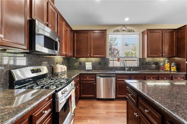 kitchen featuring appliances with stainless steel finishes, a sink, dark stone countertops, recessed lighting, and light wood-type flooring