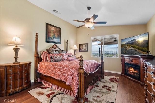 bedroom featuring visible vents, wood finished floors, baseboards, lofted ceiling, and a glass covered fireplace