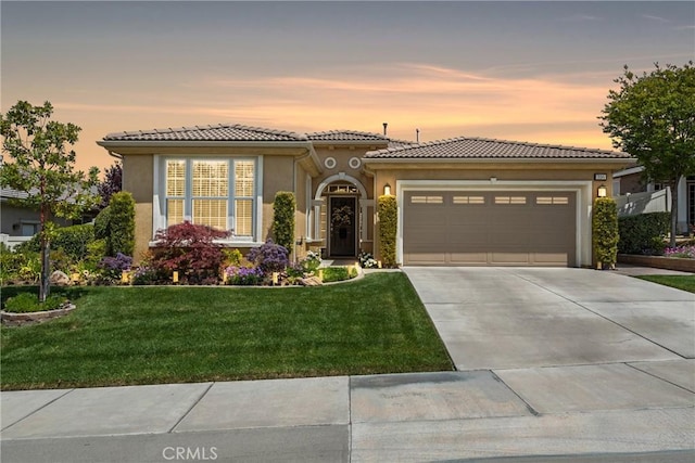 mediterranean / spanish-style home with a garage, stucco siding, a tiled roof, concrete driveway, and a lawn