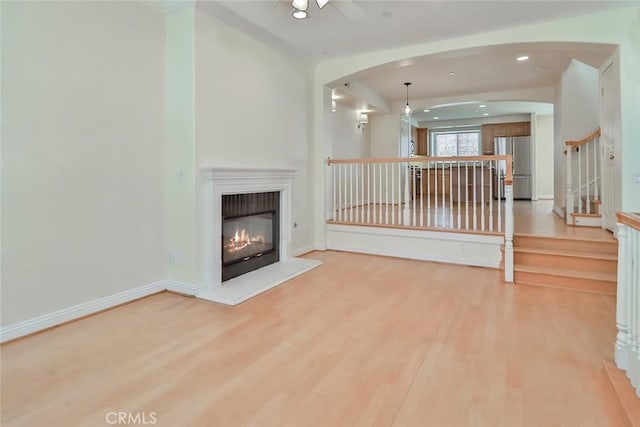 unfurnished living room with arched walkways, a glass covered fireplace, light wood-style flooring, recessed lighting, and stairway