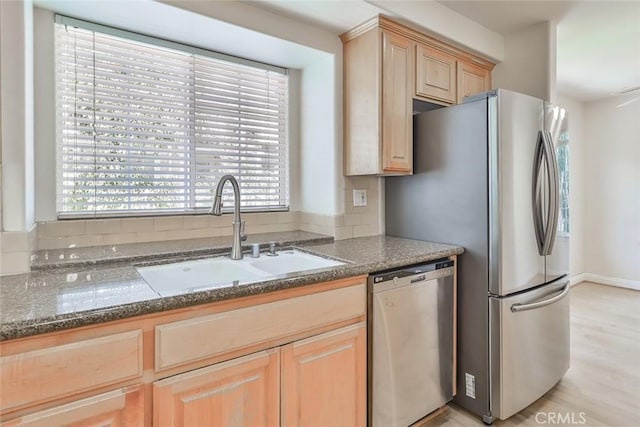 kitchen featuring stainless steel dishwasher, a sink, plenty of natural light, and light brown cabinetry