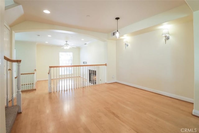 empty room featuring visible vents, a ceiling fan, wood finished floors, baseboards, and arched walkways