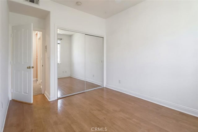 unfurnished bedroom with a closet, baseboards, wood finished floors, and visible vents