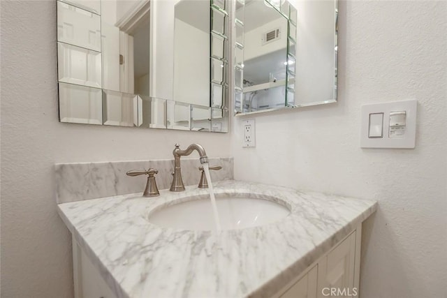 bathroom with a textured wall, visible vents, and vanity