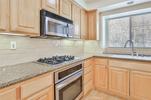 kitchen featuring light brown cabinets, stone countertops, a sink, backsplash, and stainless steel appliances