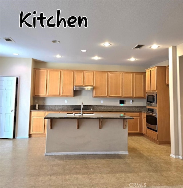 kitchen with visible vents, a breakfast bar, under cabinet range hood, a sink, and stainless steel appliances