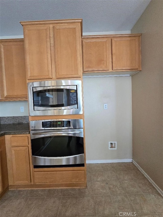 kitchen with baseboards, appliances with stainless steel finishes, tile patterned flooring, and dark countertops