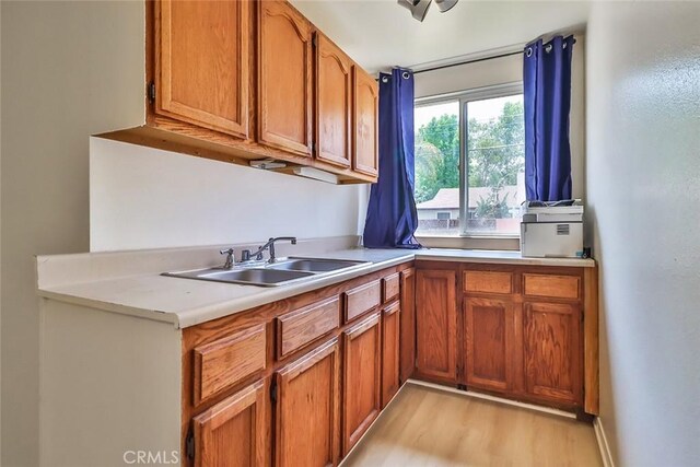 kitchen featuring light countertops, brown cabinetry, a sink, and light wood finished floors