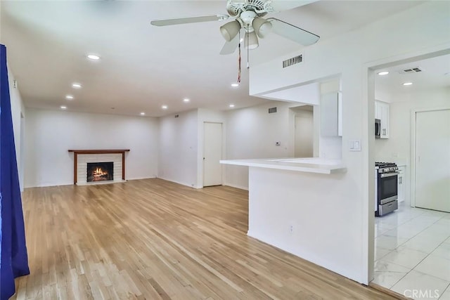 unfurnished living room with a ceiling fan, visible vents, a brick fireplace, light wood-type flooring, and recessed lighting