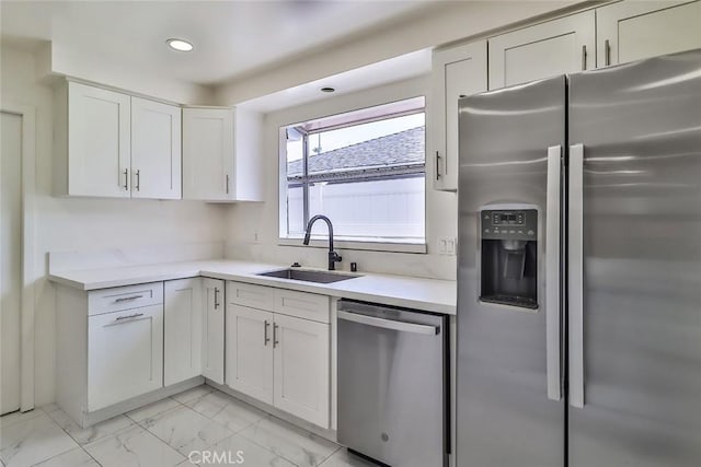 kitchen featuring appliances with stainless steel finishes, a sink, light countertops, white cabinets, and marble finish floor