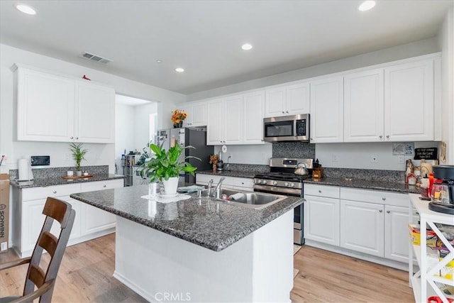 kitchen with a kitchen island with sink, stainless steel appliances, light wood finished floors, and white cabinetry