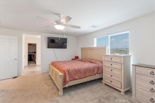 bedroom with a spacious closet, visible vents, a ceiling fan, and light colored carpet
