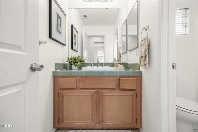 bathroom with toilet, vanity, visible vents, and plenty of natural light