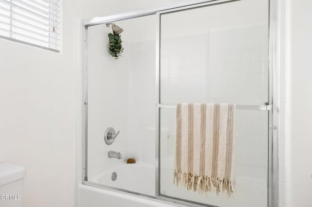 bathroom featuring toilet and shower / bath combination with glass door