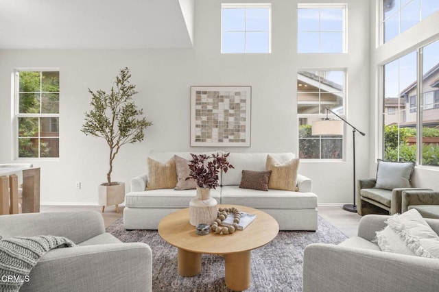 living room featuring a high ceiling, wood finished floors, baseboards, and a healthy amount of sunlight