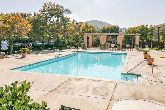community pool featuring a mountain view, a patio area, a pergola, and fence