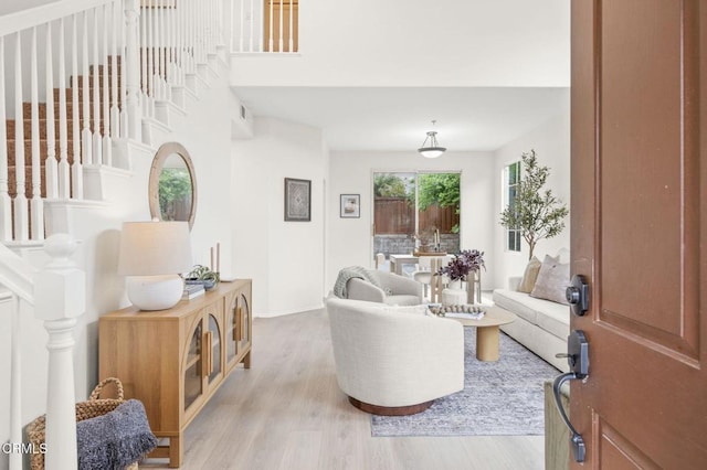 living room featuring stairway, a high ceiling, baseboards, and light wood-type flooring