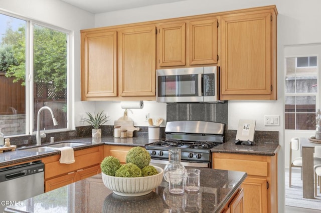 kitchen with stainless steel appliances, dark stone counters, and a sink