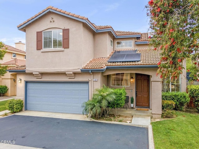 mediterranean / spanish house with a garage, stucco siding, a tile roof, aphalt driveway, and roof mounted solar panels
