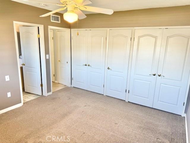 unfurnished bedroom with multiple closets, visible vents, baseboards, ceiling fan, and light carpet