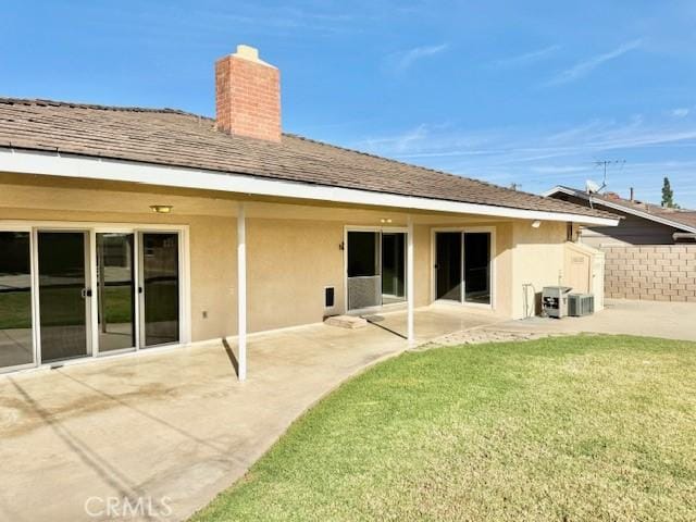back of property featuring a patio, stucco siding, a chimney, a lawn, and fence