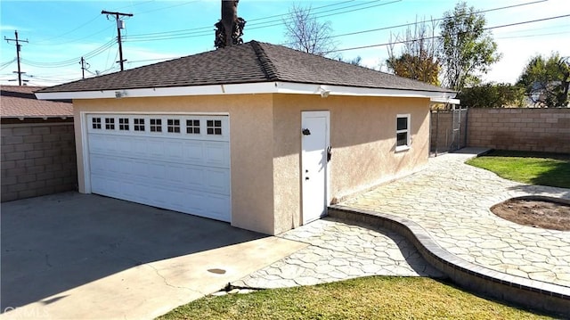 view of side of property with roof with shingles, fence, a detached garage, an outdoor structure, and stucco siding
