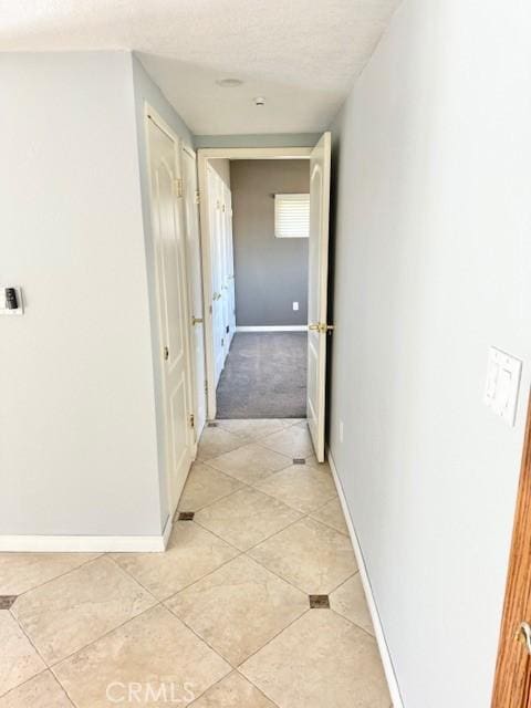 hall featuring light tile patterned flooring, a textured ceiling, and baseboards