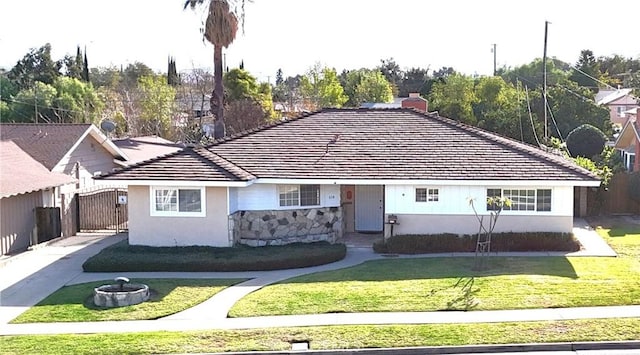 view of front of home featuring fence, stucco siding, a tile roof, stone siding, and a front lawn