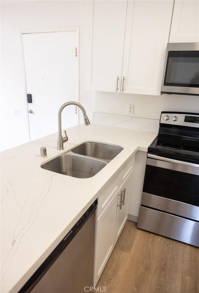 kitchen with a sink, white cabinets, stainless steel appliances, and light wood-type flooring