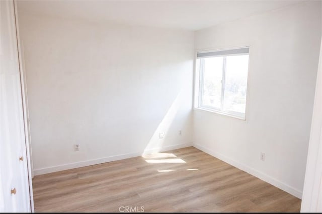 spare room with baseboards and light wood finished floors