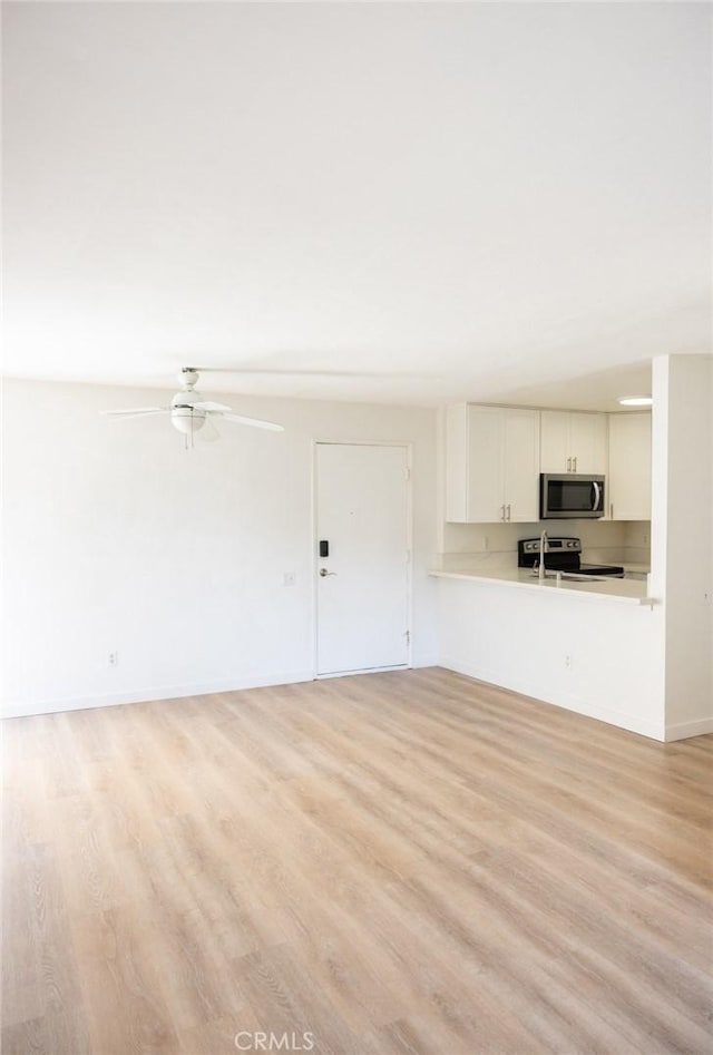 unfurnished living room featuring a ceiling fan, baseboards, and light wood-style flooring