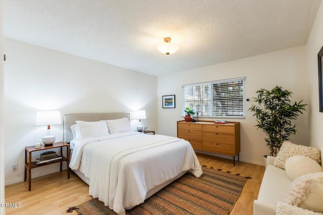 bedroom with a textured ceiling, baseboards, and light wood-style floors