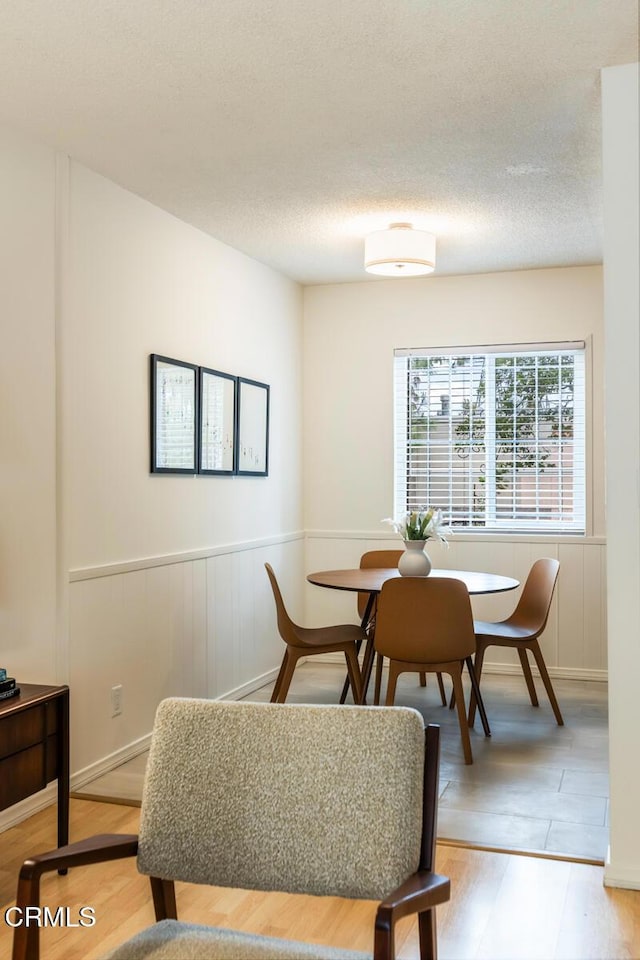 dining room featuring a decorative wall, light wood-type flooring, and a wainscoted wall