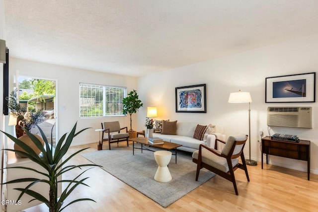 living area with an AC wall unit, light wood-style flooring, and baseboards