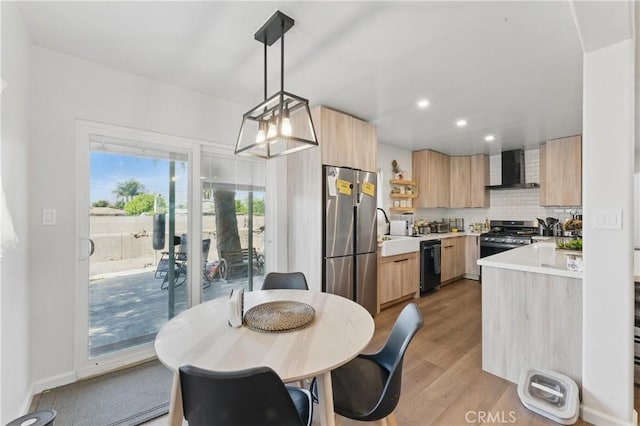 kitchen with wall chimney range hood, light brown cabinets, light countertops, stainless steel appliances, and modern cabinets