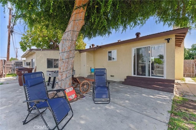 rear view of property featuring entry steps, fence, a patio, and stucco siding