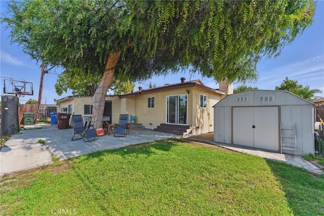 back of property featuring a lawn, a patio area, an outdoor structure, a storage unit, and stucco siding