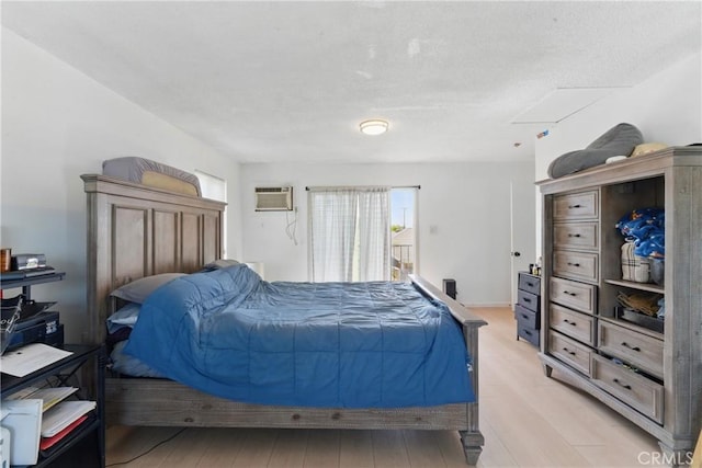 bedroom featuring a wall mounted air conditioner, light wood-style flooring, and a textured ceiling