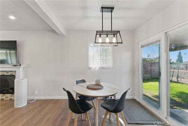 dining area featuring baseboards, a brick fireplace, wood finished floors, and beam ceiling