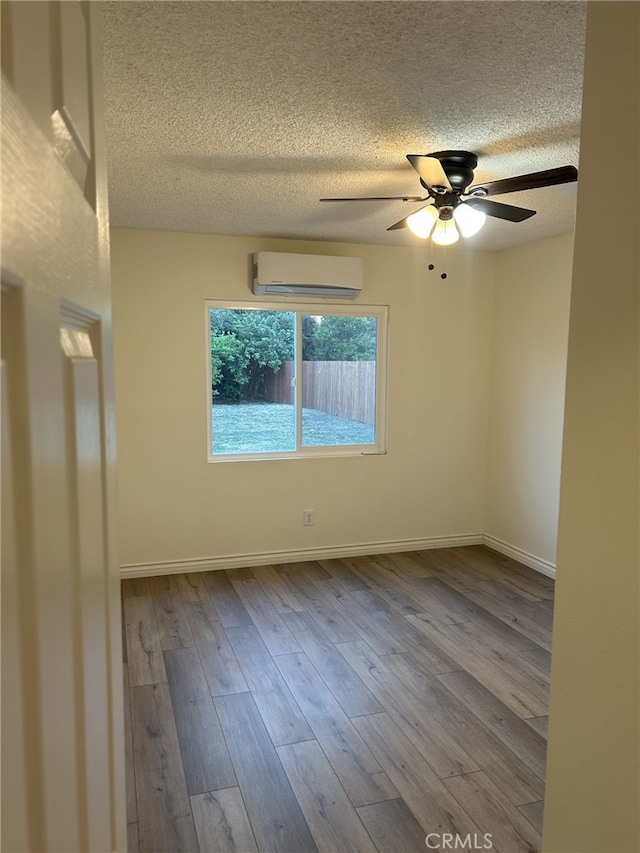 unfurnished room featuring a wall mounted air conditioner, a textured ceiling, ceiling fan, wood finished floors, and baseboards